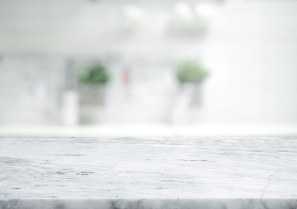 A clean white marble countertop in focus with a blurred, bright kitchen background.