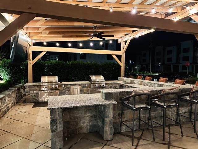 Outdoor kitchen at night featuring a bar area with seating, illuminated by soft lighting for a cozy atmosphere